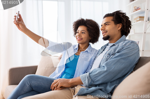 Image of happy couple with smartphone taking selfie at home