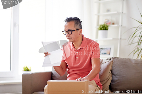 Image of man with parcel box reading invoice at home