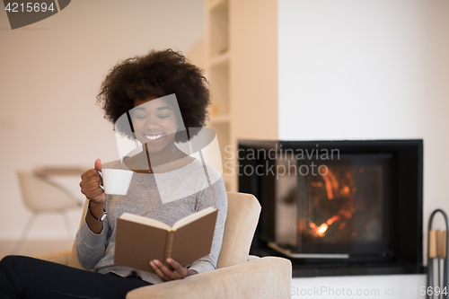 Image of black woman reading book  in front of fireplace