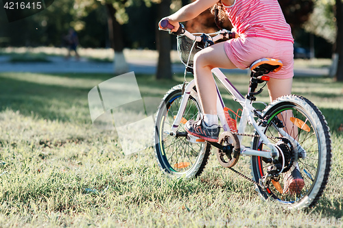 Image of Little brunette girl riding bicycle in the park at sunset