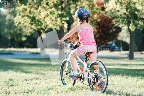 Image of Little brunette girl riding bicycle in the park at sunset