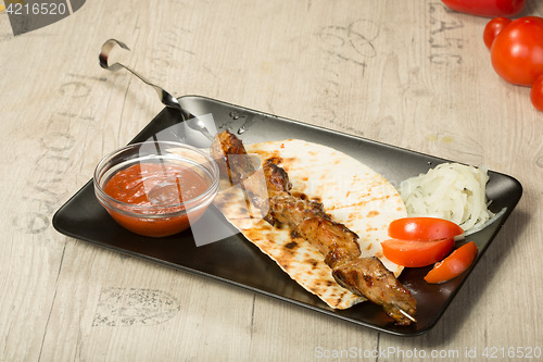 Image of shashlik. kebab skewer, black rectangular plate. sauce and onions