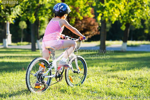 Image of happy child girl riding bicycle in summer sunset