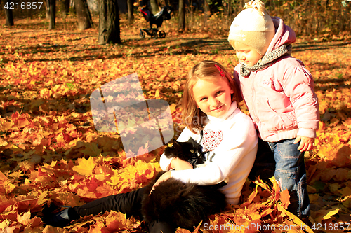 Image of sisters play with cat in the autumn park