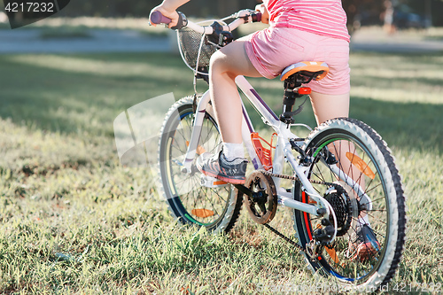 Image of Little brunette girl riding bicycle in the park at sunset
