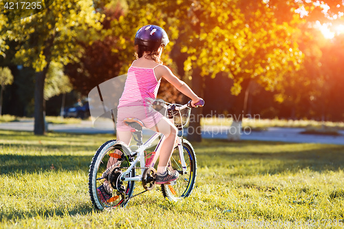 Image of child girl riding bicycle on summer sunset in the park.