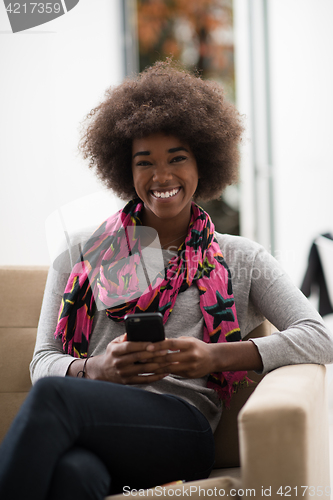 Image of black woman sitting on sofa and using mobile phone