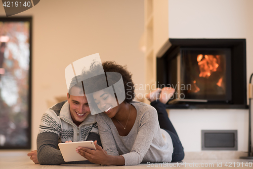 Image of multiethnic couple using tablet computer on the floor