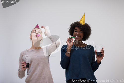 Image of smiling women in party caps blowing to whistles