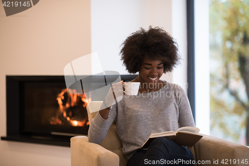 Image of black woman reading book  in front of fireplace