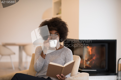 Image of black woman reading book  in front of fireplace