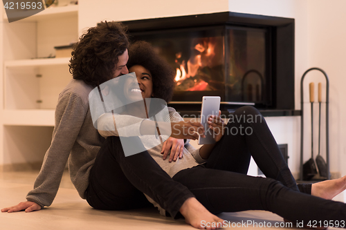 Image of multiethnic couple using tablet computer on the floor