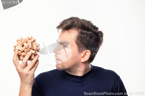 Image of Attractive 25 year old business man looking confused at wooden puzzle.