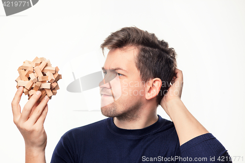 Image of Attractive 25 year old business man looking confused at wooden puzzle.