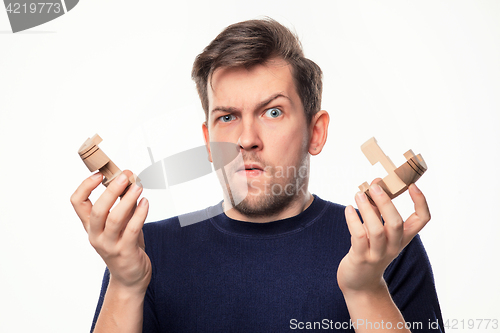Image of Attractive 25 year old business man looking confused with wooden puzzle.