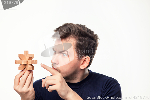 Image of Attractive 25 year old business man looking confused at wooden puzzle.