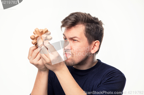 Image of Attractive 25 year old business man looking confused at wooden puzzle.