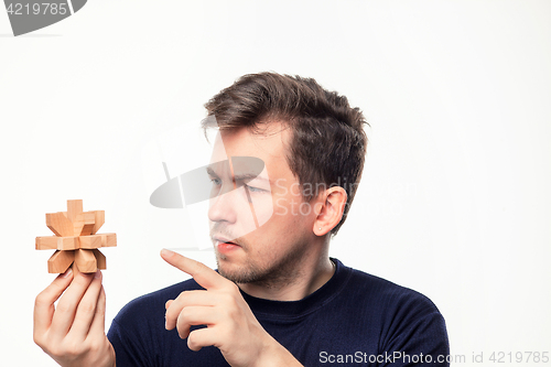 Image of Attractive 25 year old business man looking confused at wooden puzzle.