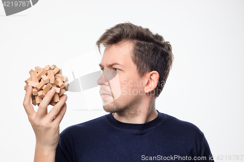 Image of Attractive 25 year old business man looking confused at wooden puzzle.