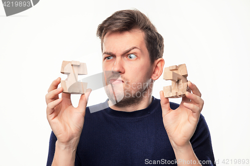 Image of Attractive 25 year old business man looking confused at wooden puzzle.