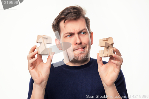 Image of Attractive 25 year old business man looking confused at wooden puzzle.