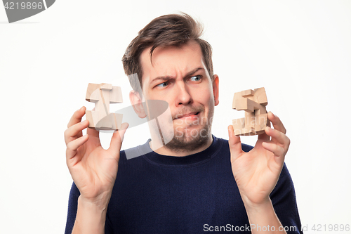 Image of Attractive 25 year old business man looking confused at wooden puzzle.