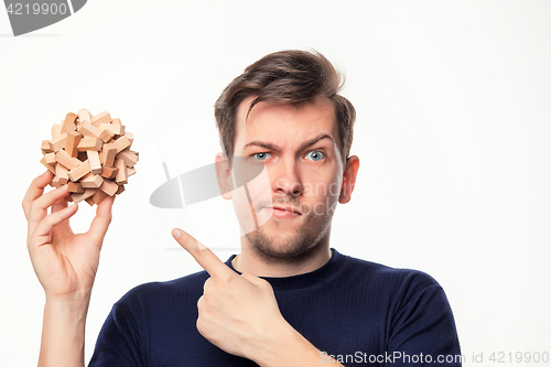 Image of Attractive 25 year old business man looking confused with wooden puzzle.