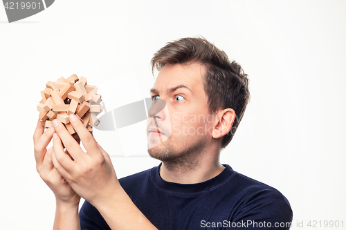 Image of Attractive 25 year old business man looking confused at wooden puzzle.