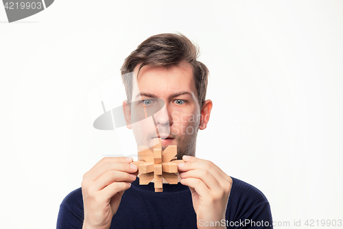 Image of Attractive 25 year old business man looking confused at wooden puzzle.
