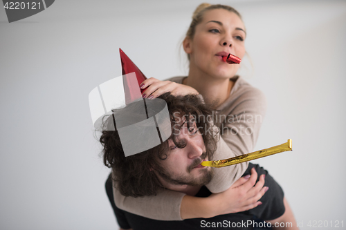 Image of couple in party hats blowing in whistle