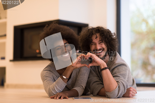 Image of multiethnic couple showing a heart with their hands on the floor