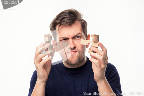 Image of Attractive 25 year old business man looking confused with wooden puzzle.