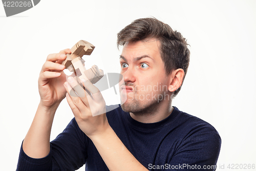 Image of Attractive 25 year old business man looking confused with wooden puzzle.