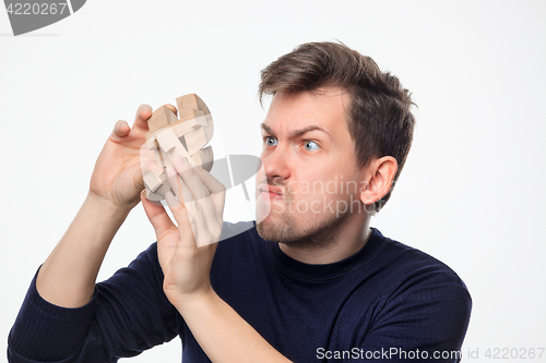 Image of Attractive 25 year old business man looking confused with wooden puzzle.