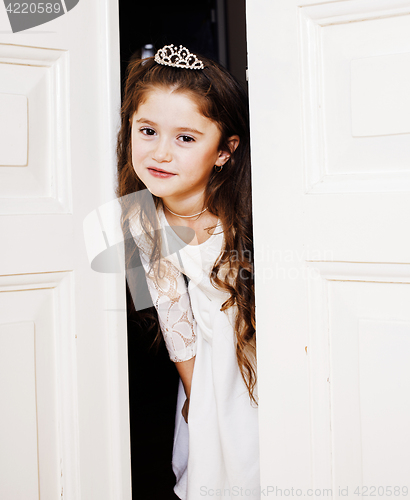 Image of little cute girl at home, opening door well-dressed in white dress and tiara, adorable milk fairy teeth