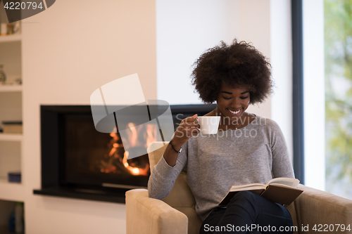 Image of black woman reading book  in front of fireplace