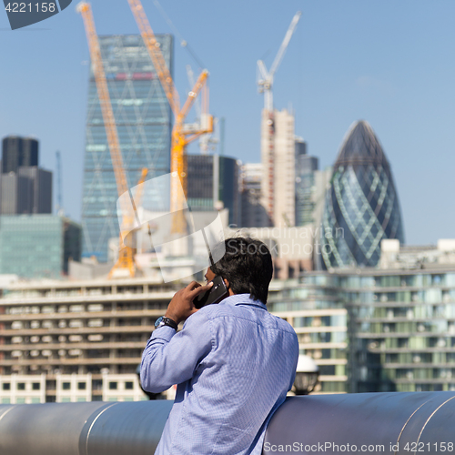 Image of International businessman talking on mobile phone outdoor in London city, UK.