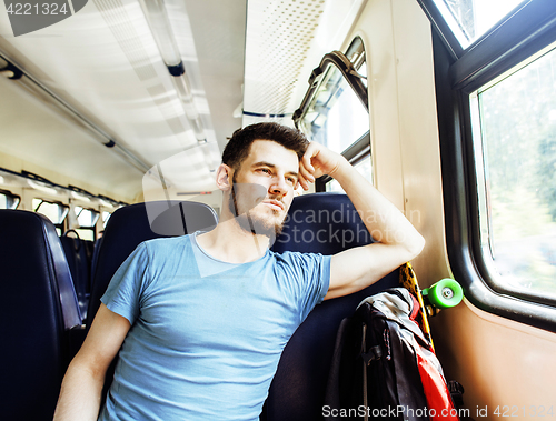 Image of young pretty modern hipster guy traveller on train with skateboard alone, lifestyle vacation people concept close up smiling cool