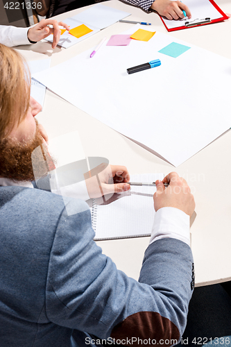 Image of The man sitting behind desk, checking reports, talking.