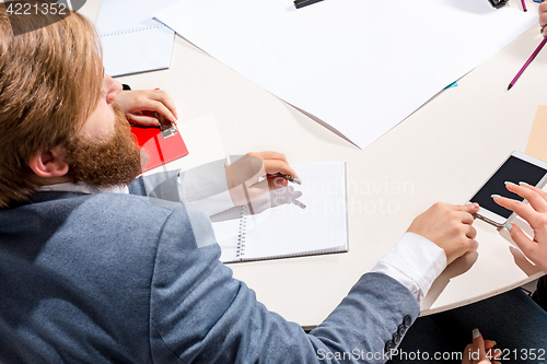 Image of The man sitting behind desk, checking reports, talking.