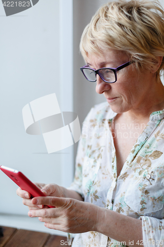 Image of Mature female in glasses using smartphone