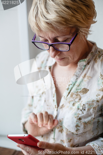 Image of Mature female in glasses using smartphone