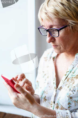 Image of Mature female in glasses using smartphone