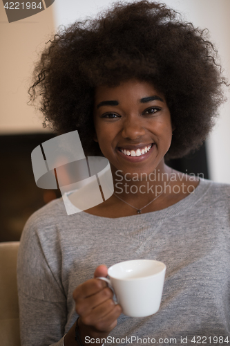 Image of black woman drinking coffee in front of fireplace