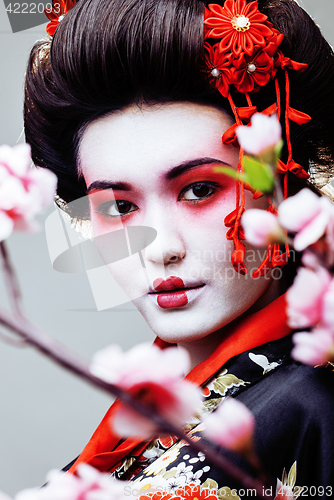 Image of young pretty geisha in black kimono among sakura, asian ethno close up