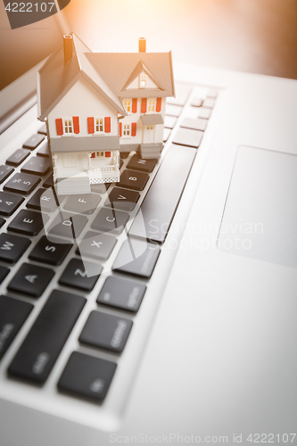 Image of Miniature House And Laptop Computer Resting on Desktop.