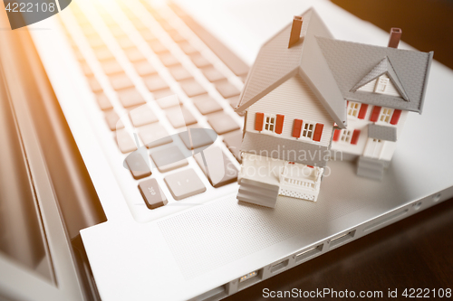 Image of Miniature House And Laptop Computer Resting on Desktop.