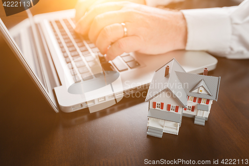 Image of Miniature House Resting on Desktop And Man Using Laptop Computer