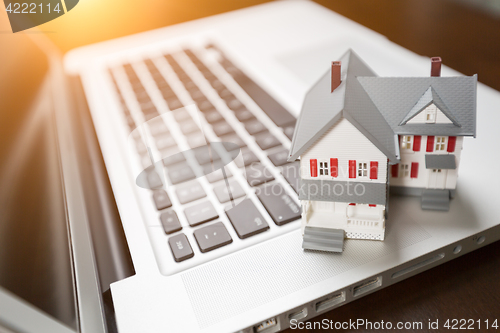 Image of Miniature House And Laptop Computer Resting on Desktop.