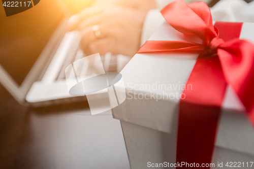Image of White Gift Box with Red Ribbon and Bow Near Man Typing on Laptop